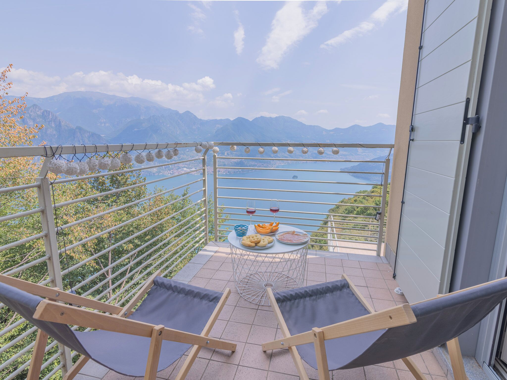 A balcony with a view of mountains, a table with food and drinks, and a hammock.