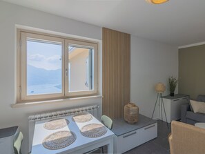 A modern kitchen with a large window, a dining table with placemats, and a view of the sea. - EnjoyIseoLake - Lake Serenity (Plassi)