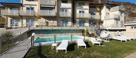 Un edificio de varios pisos con balcones, una piscina y sillones de exterior.