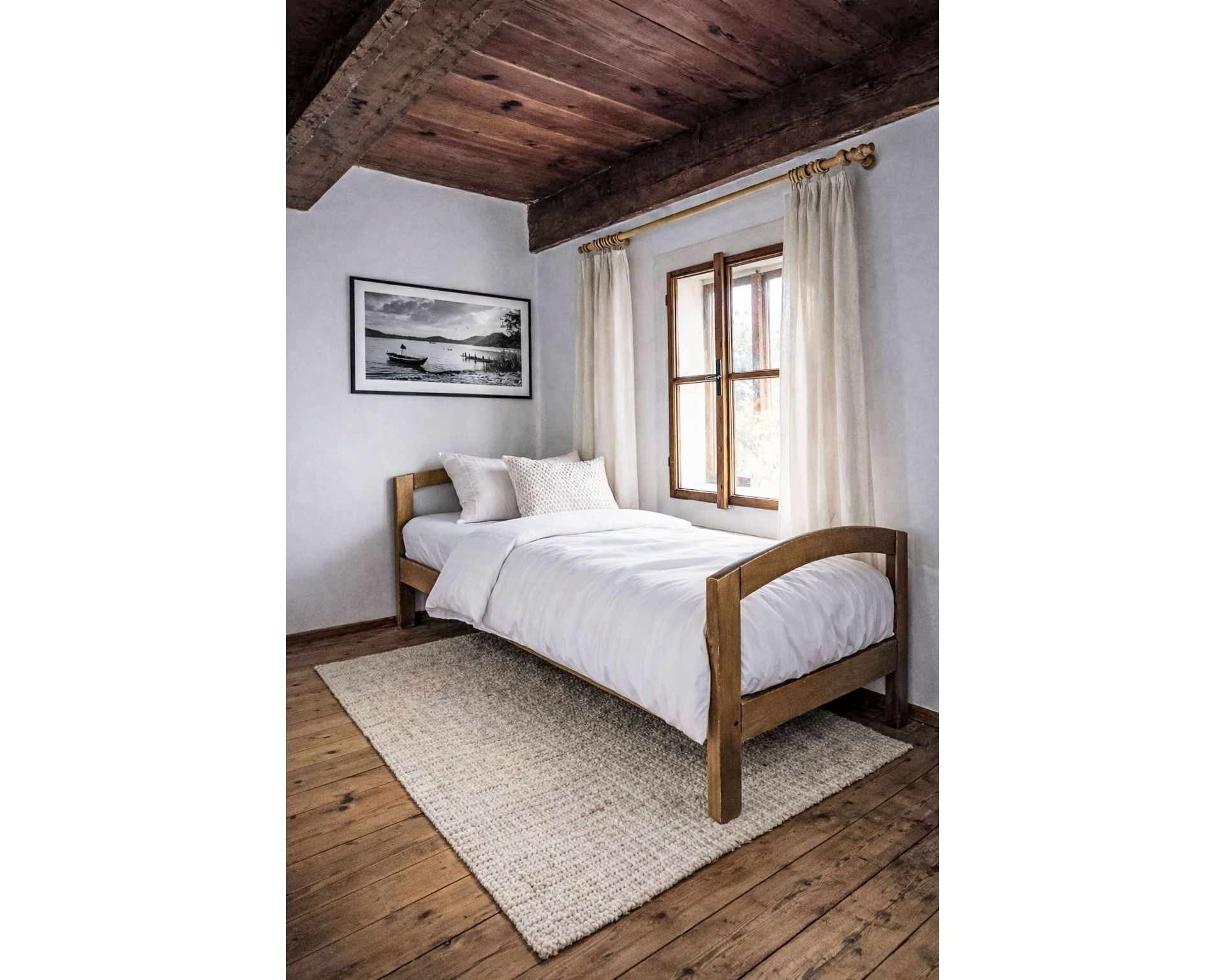A bed with a wooden frame, white bedding, and a rug on a wooden floor.