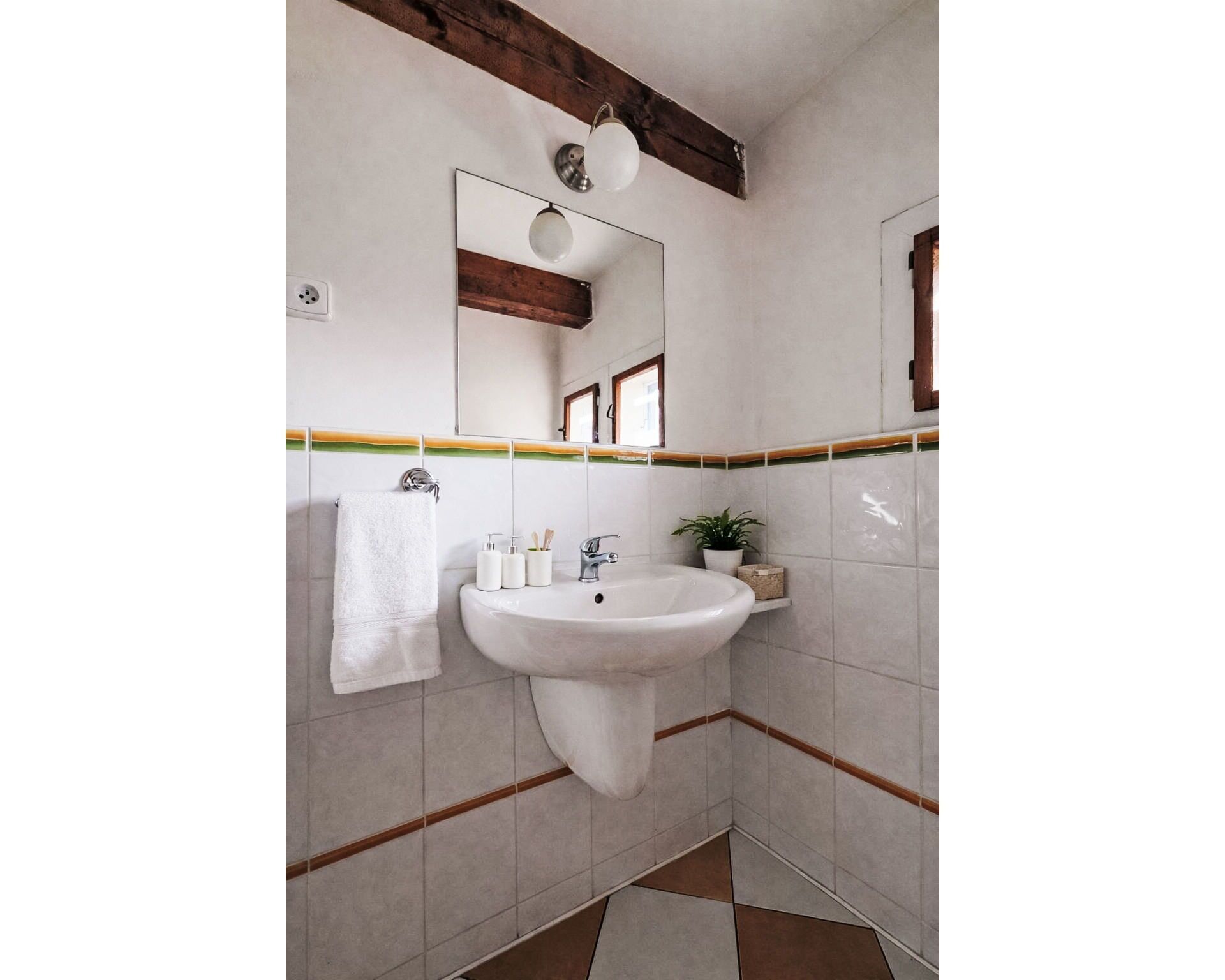 Une salle de bain avec un lavabo blanc, une serviette, un miroir et une plante en pot.