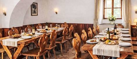 Comedor con mesas y sillas de madera, manteles blancos y copas de vino.