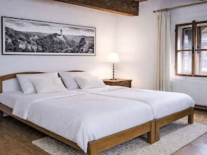 Un dormitorio con una cama grande, una lámpara de noche, una ventana con cortinas y un cuadro de paisaje enmarcado en la pared.