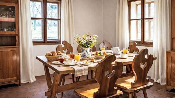 A dining area with a wooden table set for breakfast, surrounded by chairs with heart-shaped backrests.