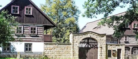 A two-story wooden house with a stone entrance and a fenced yard.