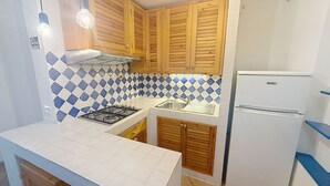 Eine kleine Küche mit Holzschränken, einem Gasherd, einer Spüle und einem weißen Kühlschrank.