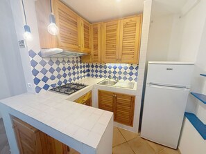 Eine kleine Küche mit Holzschränken, einem Gasherd, einer Spüle und einem weißen Kühlschrank.