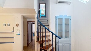 Eine Treppe mit blauer Handlauf, die zu einer Zwischenebene führt, ein blauer Stuhl und eine weiße Tür mit Glasfeldern.
