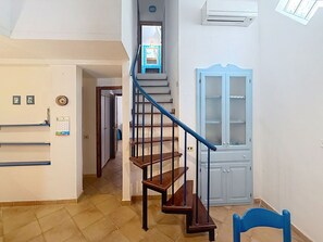Eine Treppe mit blauer Handlauf, die zu einer Zwischenebene führt, ein blauer Stuhl und eine weiße Tür mit Glasfeldern.