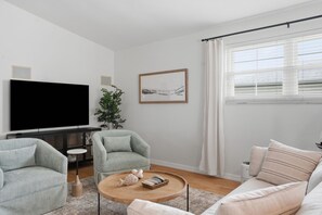 Ein modernes Wohnzimmer mit Fernseher, zwei Sesseln, einem runden Couchtisch und einer Couch.