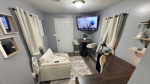 Un espacio habitable compacto con un sofá, una pequeña mesa de comedor, un televisor montado en la pared y una puerta.