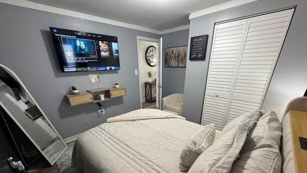 Un dormitorio con cama, televisor montado en la pared, mesita de noche y armario.