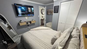 Ein Schlafzimmer mit Bett, Wandfernseher, Nachttisch und Kleiderschrank.