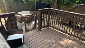 Terraza de madera con barandilla, muebles de mimbre y una pequeña mesa.