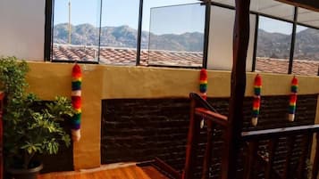 A balcony with a view of mountains, a potted plant, and a wooden railing.
