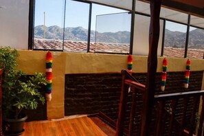 Un balcón con vistas a las montañas, una planta en maceta y una baranda de madera.