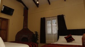 Habitación de hotel con dos camas, chimenea, televisor y ventana con cortinas.