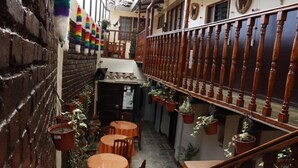 Un callejón estrecho con mesas y sillas, plantas en macetas y una barandilla de madera.