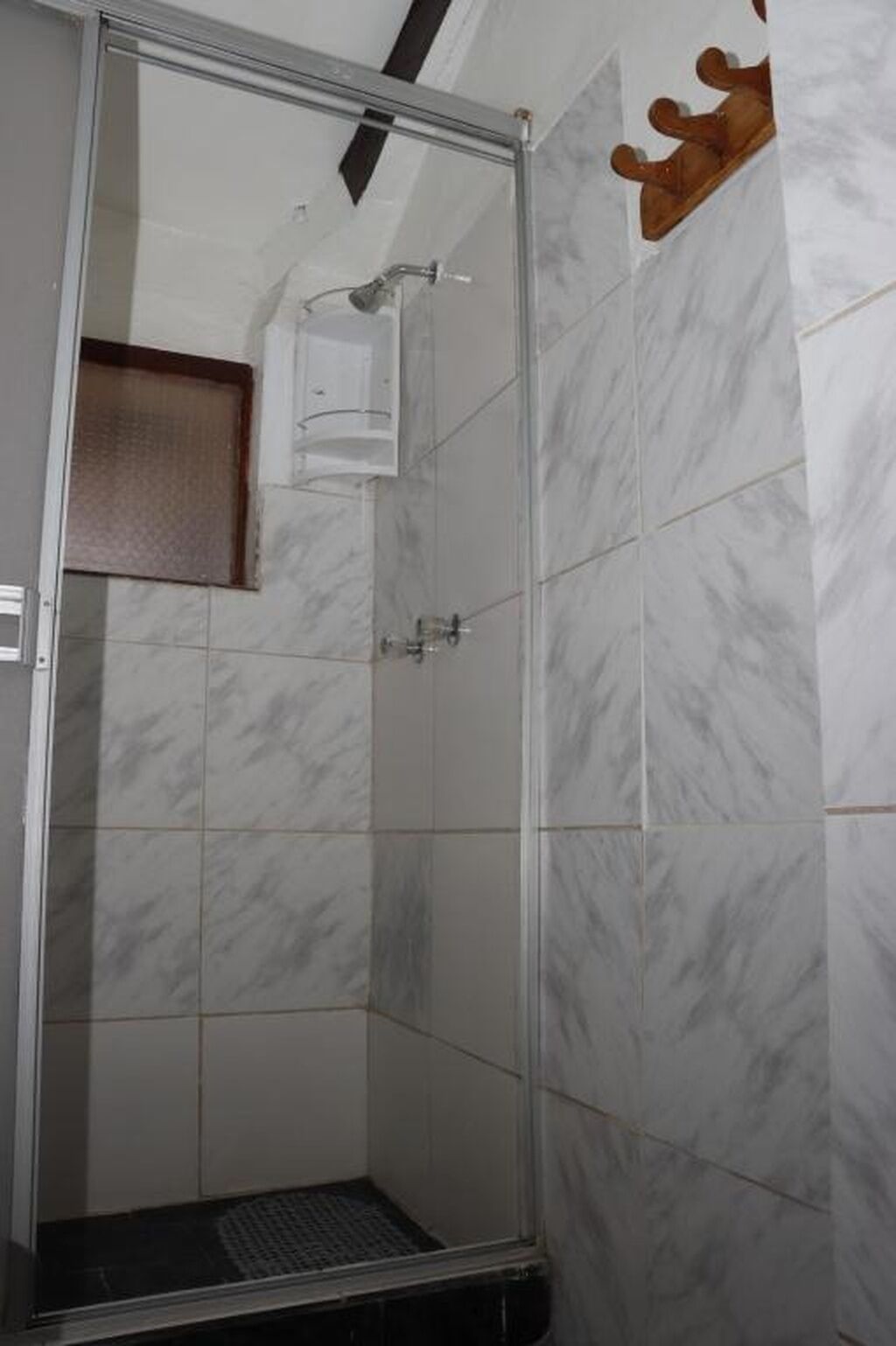 Una ducha con paredes de vidrio, piso de baldosas y un pequeño estante sobre la puerta.
