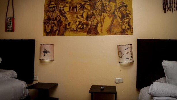 A hotel room with two beds, a wall mural, and two wall-mounted clocks. - Casona Terrazas Inn (Cusco)