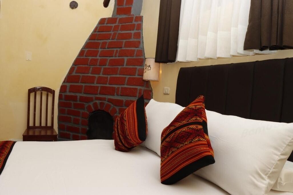 Una habitación de hotel con chimenea de ladrillo, una cama con ropa de cama blanca y una ventana con cortinas.