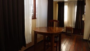 A room with a wooden dining table and chairs, a small side table, and a window with curtains. - Casona Terrazas Inn (Cusco)