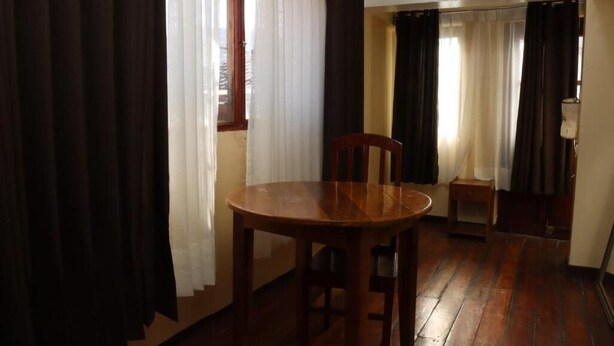 Una habitación con una mesa de comedor de madera, sillas, una mesita auxiliar y una ventana con cortinas.