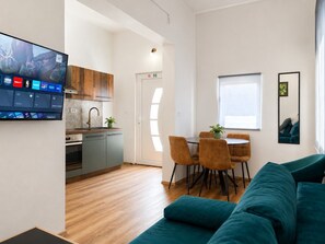 Ein zeitgemäßer Wohnraum mit Küche, Essbereich und einem großen Flachbildfernseher an der Wand.