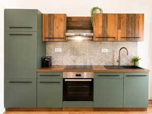 Een keuken met groene kastjes, een roestvrijstalen oven, een koffieapparaat en een houten achterwand.
