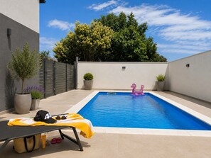 Ein Schwimmbecken mit einem kleinen Luftspielzeug, einer Liege und Topfpflanzen.