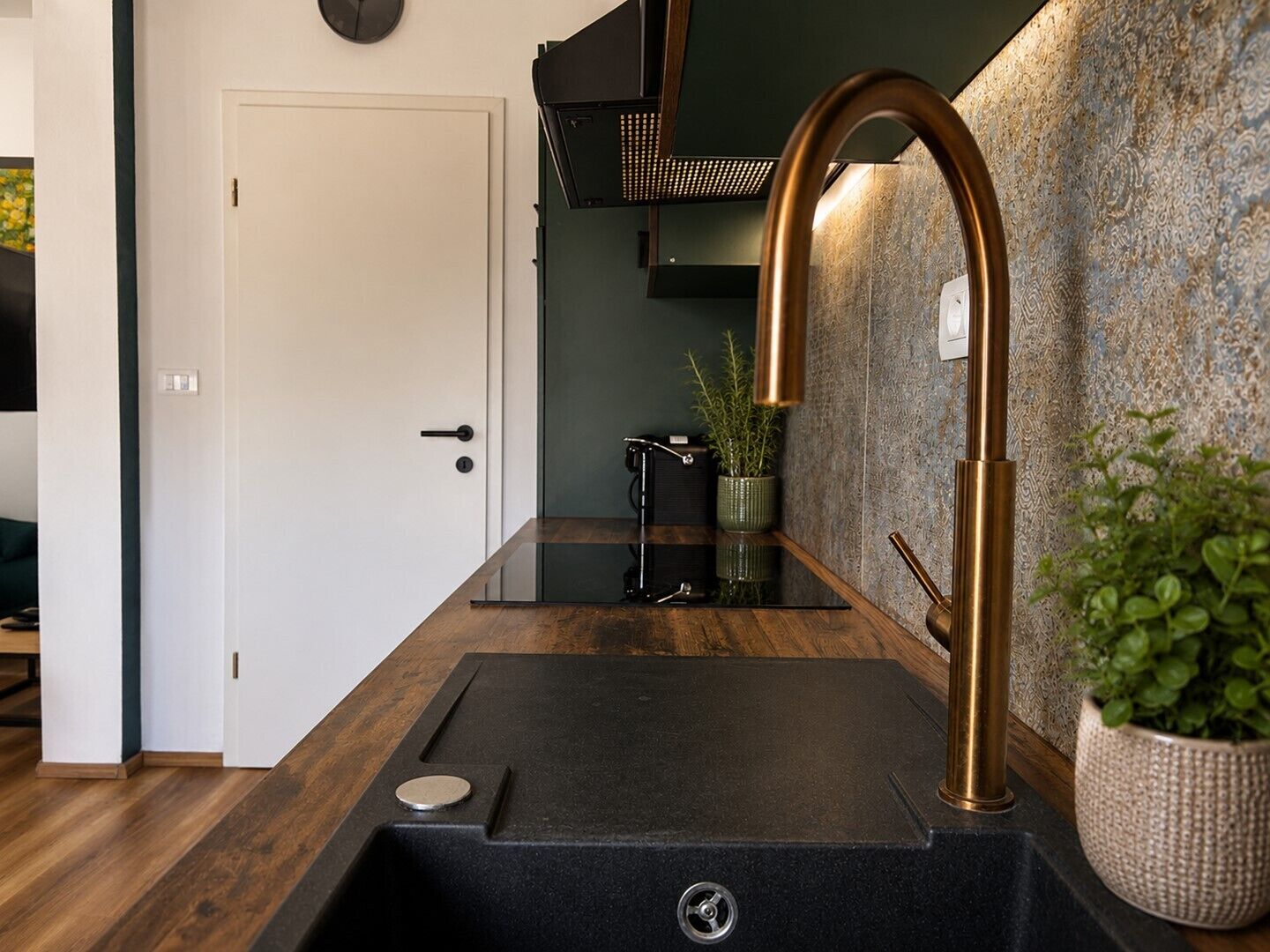 A modern kitchen with a black countertop, a copper faucet, and a potted plant.