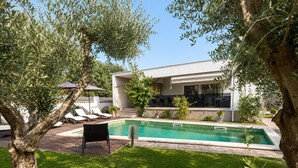 Ein moderner Poolbereich im Freien mit Liegestuhl, kleinem Tisch und einem Gebäude mit großen Fenstern.