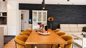 Eine moderne Küche mit weißen Schränken, einer schwarzen Spritzschutzwand und einem Essbereich mit einem Holztisch und gelben Stühlen.