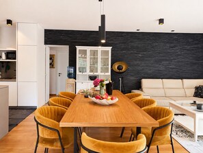 A modern kitchen with white cabinets, a black backsplash, and a dining area with a wooden table and yellow chairs. - Holiday House Pool Retreat (Pomer)