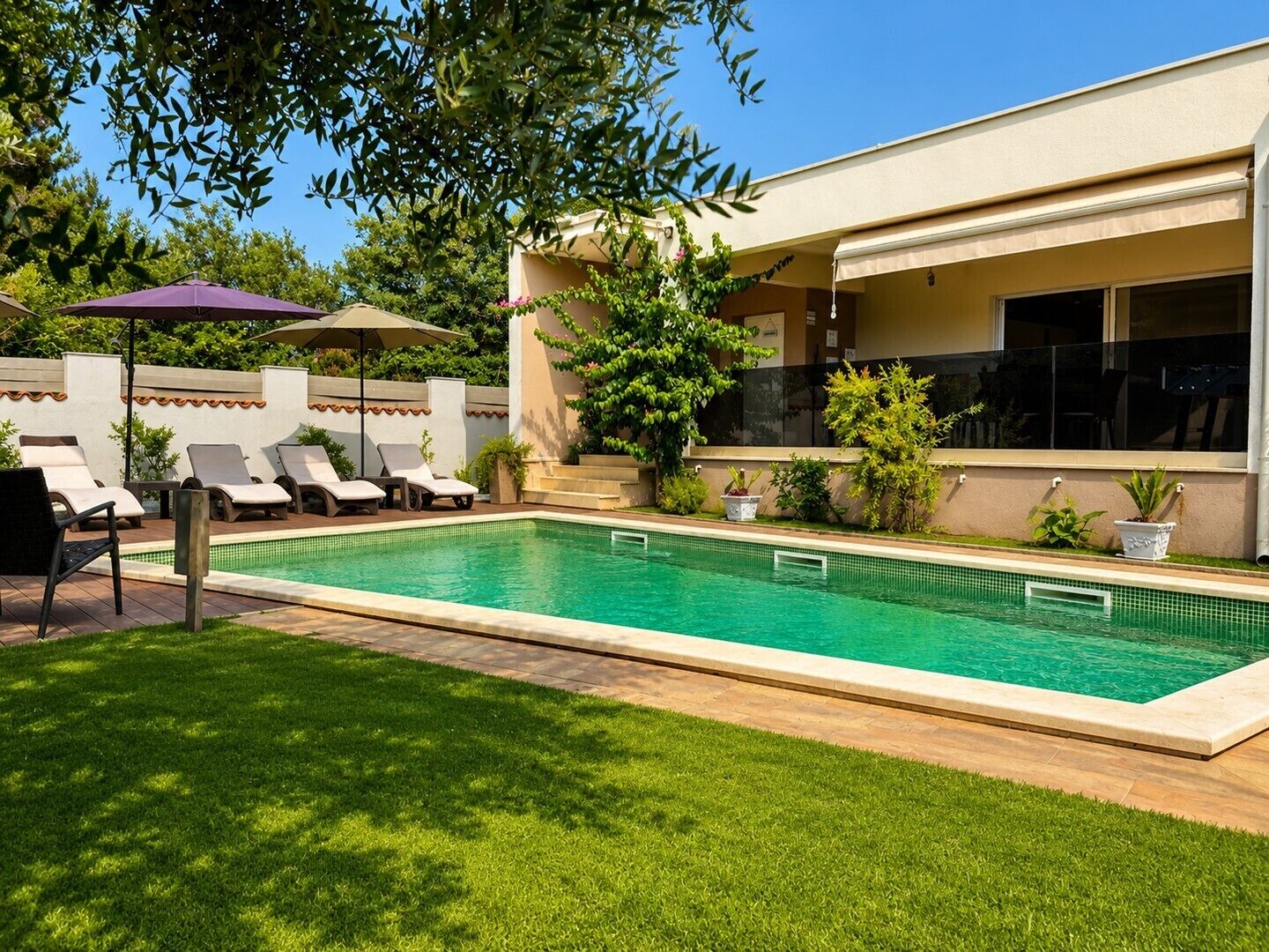 A swimming pool with lounge chairs and a covered area, surrounded by greenery and a building.