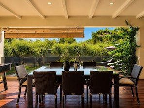 An outdoor dining area with a glass table and wicker chairs, overlooking a garden with trees and a pergola. - Holiday House Pool Retreat (Pomer)