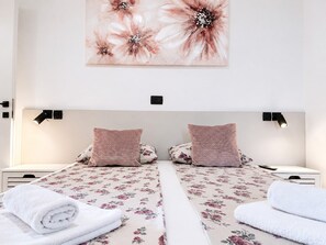 A double room with two beds, each with a floral bedspread, two bedside tables, and two wall-mounted lamps. - Holiday House Pool Retreat (Pomer)