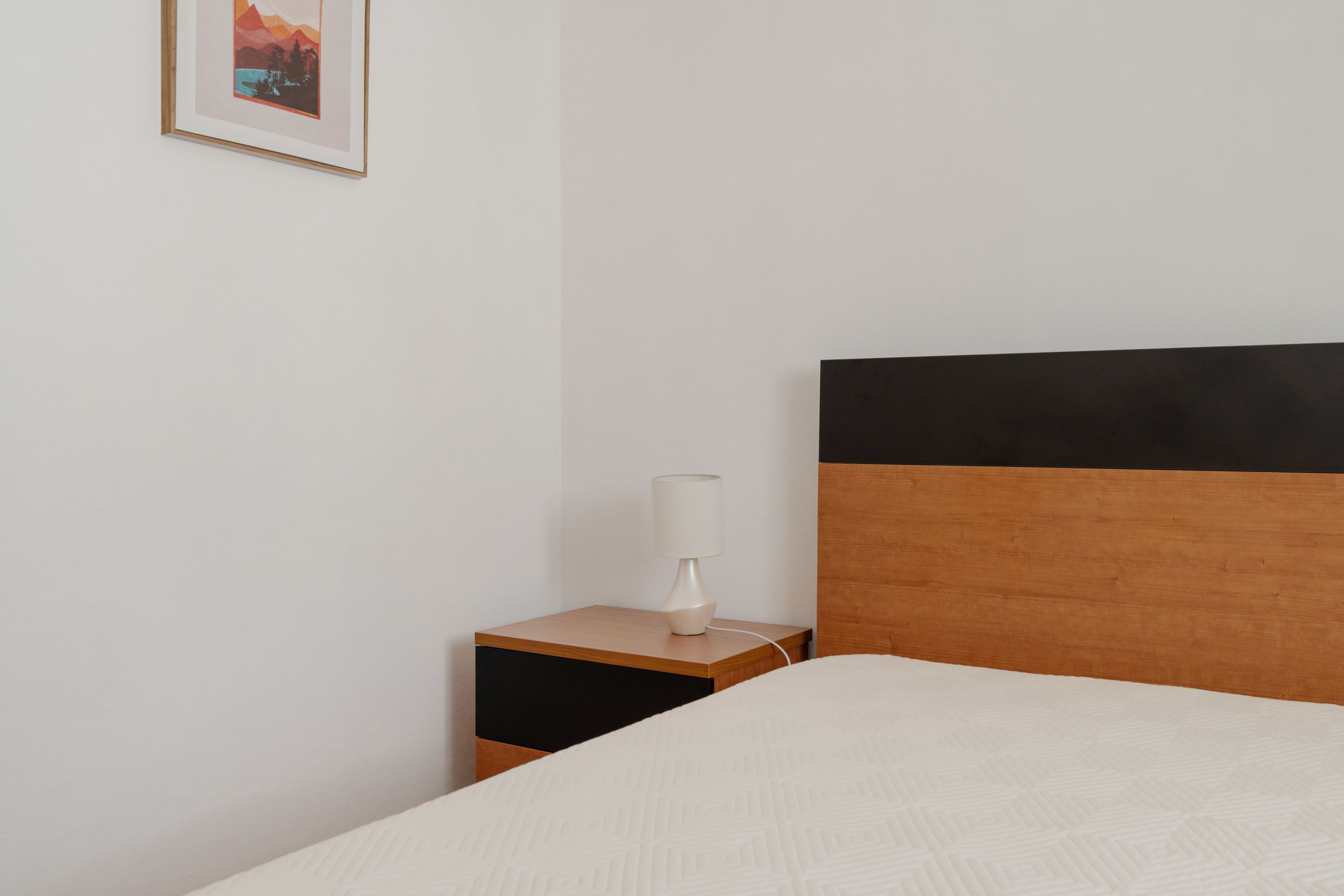 Una cama bien hecha con edredón blanco y cabecera de madera con detalles negros.