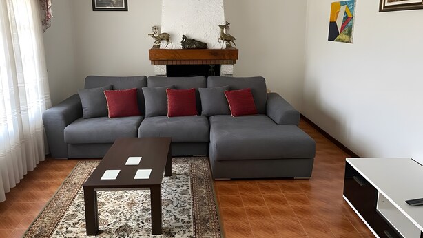 A living room with a grey sofa, red cushions, a wooden coffee table, and a fireplace with decorative items. - Vivenda Ribeiro: House with Mountain View, Private Pool and Wi-Fi (Curvos)