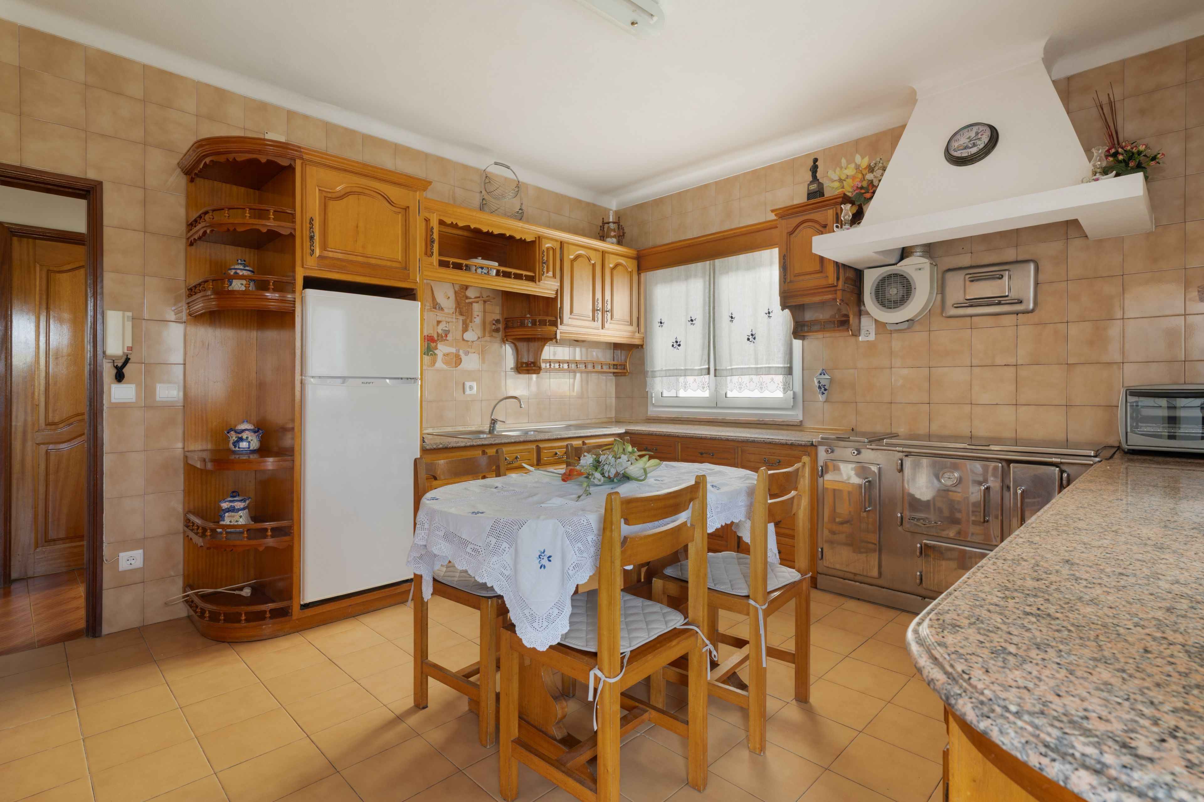 Una cocina con armarios de madera, un refrigerador, un lavamanos y una mesa de comedor con sillas.