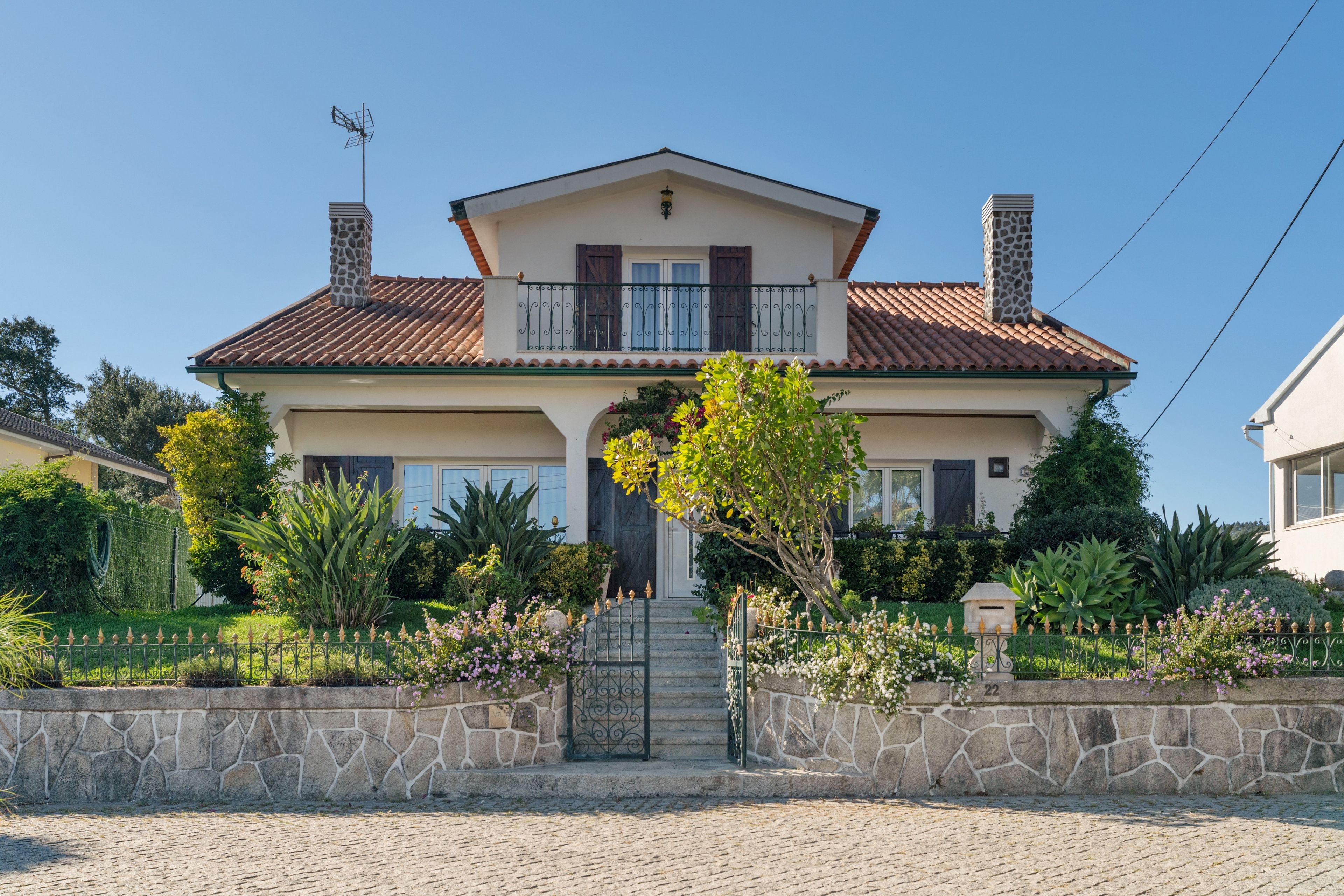 A two-story house with a tiled roof, a central entrance with steps, and a stone wall in front.