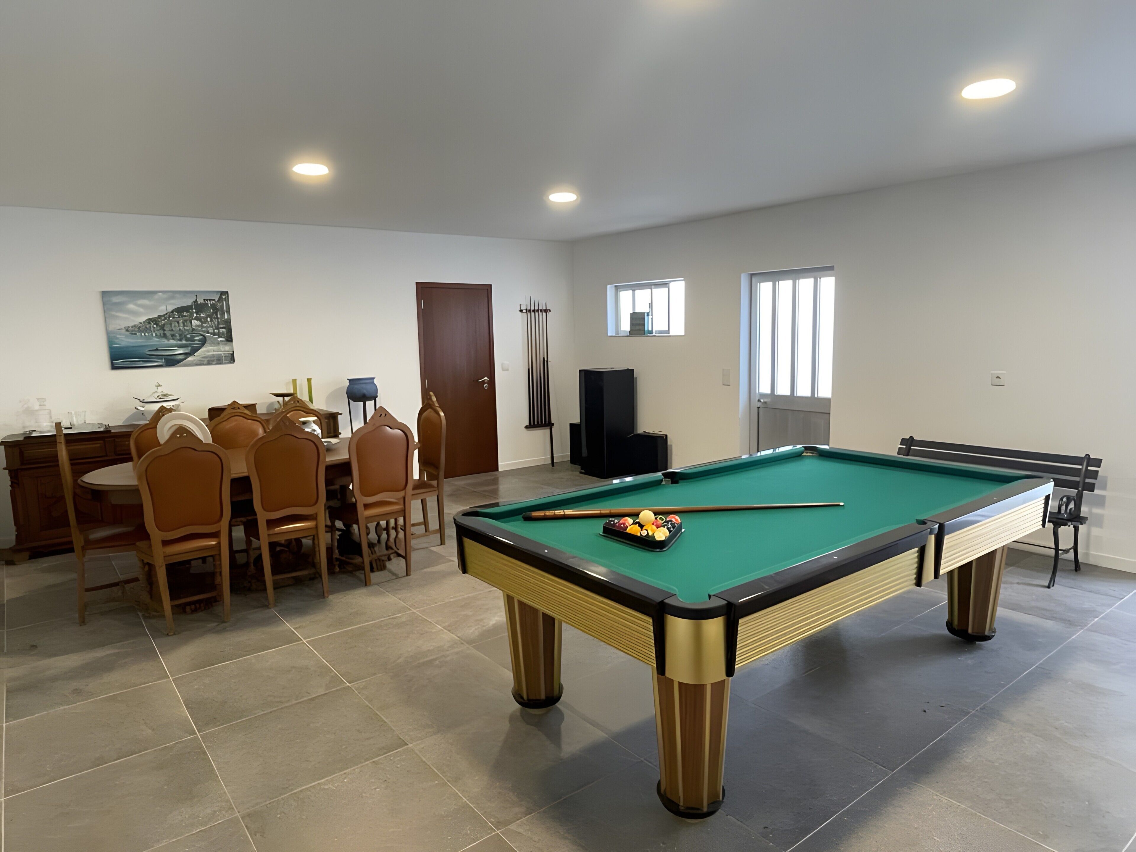 Une table de billard avec des billes, une table à manger avec des chaises et un tableau accroché au mur.