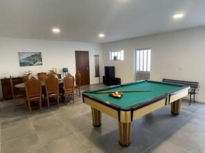 Una mesa de billar con bolas, una mesa de comedor con sillas y un cuadro en la pared.