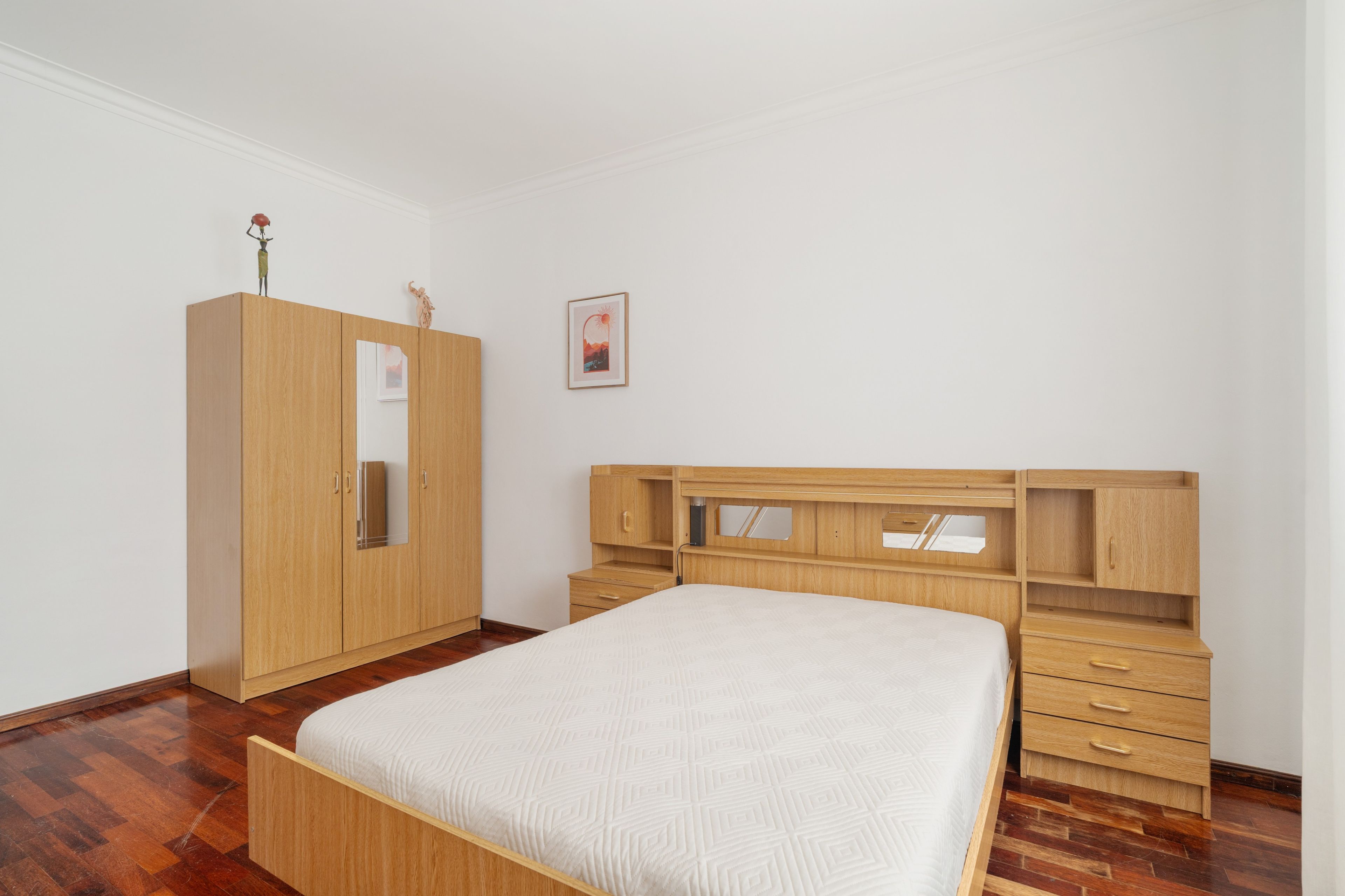 A bedroom with a wooden bed, a wardrobe, and a desk with drawers.