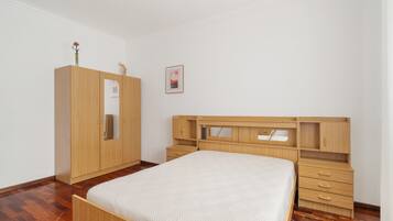 A bedroom with a wooden bed, a wardrobe, and a desk with drawers.