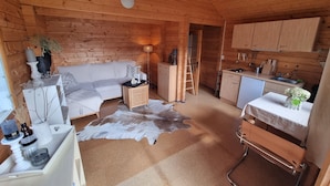 Interior acollidor d'una cabana amb sostre de fusta, un sofà, una taula de dinar, una cuina i una escala.