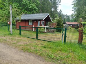 A wooden cabin with a fenced yard, surrounded by trees.