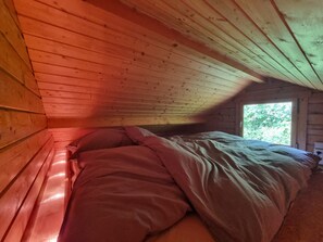 A single bed in a cabin with a sloped ceiling and a window.