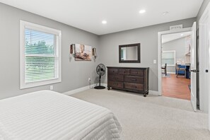 A bedroom with a bed, a dresser, a fan, and a window with blinds.