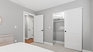 Un dormitorio con cama, cómoda y dos puertas blancas que dan a un armario y otra habitación.